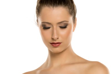 Kahverengi saçlı, makyajlı, gözleri kapalı ve aşağı bakan beyaz arka planda genç bir kadının stüdyo fotoğrafı.