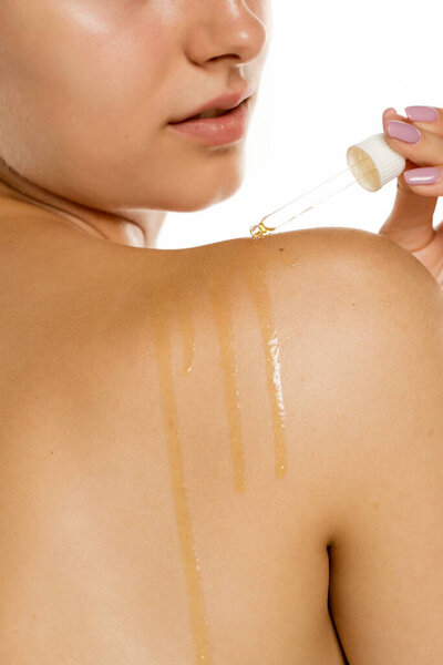 Студийный снимок молодой женщины, применяющей сыворотку к плечу с капельницей на белом фоне