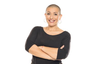 Beyaz arka planda kollarını kavuşturmuş, siyah elbiseli, kel, gülümseyen bir kadının stüdyo fotoğrafı.