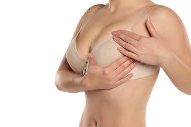 Bej renkli sutyen giymiş, göğüslerini muayene eden, beyaz arka planda göğüsleri olan bir kadının stüdyo fotoğrafı.
