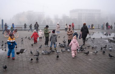 Uzhhorod, Ukraine - December 25, 2022: Chilldren playing with pigeons outdoors in Uzhhorod, Ukraine