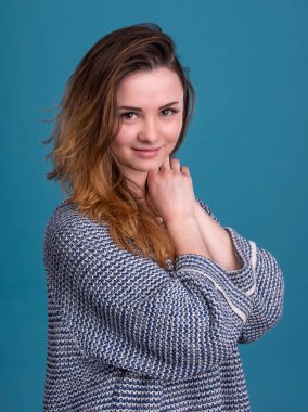 Gülümseyen genç kadın stüdyoda mavi arka planda poz veriyor.