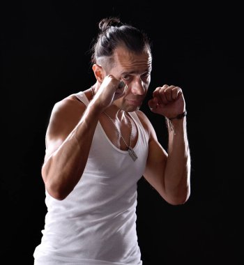 Beyaz tişörtlü yakışıklı stüdyoda siyah arka planda poz veriyor.