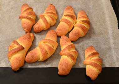 Parlak kabuklu dokuz altın sarısı kruvasan sıcak bir mutfakta parşömen kağıdıyla kaplı bir yemek tepsisinde soğuyor. Sıcak koku havayı dolduruyor.