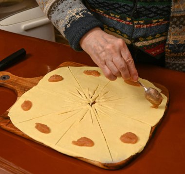 Kadın yıldız desenli hamuru ustalıkla hazırlıyor, sıcak bir mutfağı doldurmak için kaşık dolusu meyve ekliyor, ev yapımı rahatlık ve gelenek hissi uyandırıyor..