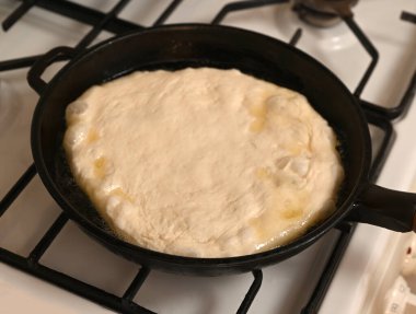 Maya hamuru gaz sobasındaki dökme demir tavada şişiyor. Bu da pişirme ilerlemesini gösteriyor. Ilık güneş ışığı mutfağı aydınlatır, rahat bir atmosfer yaratır.