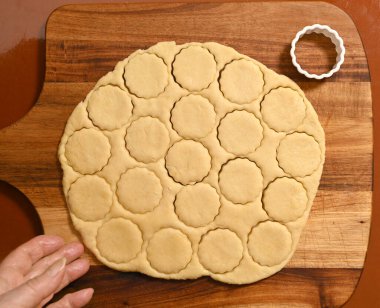 Kurabiye hamuru, ahşap bir tahtanın üzerinde ustalıkla daireler şeklinde kesilir. Yakınlarda, küçük bir kesicinin lezzetli ikramlar için daha fazla hamur şekillendirme sırası bekliyor.