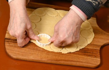 Sıcak bir mutfakta ahşap bir yüzey üzerinde hamurdan kurabiye şekilleri kesmekte ustaca çalışan bir kadın geleneksel pişirme sürecini sergiliyor.