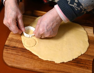 Sıcak bir mutfakta ahşap bir yüzey üzerinde hamurdan kurabiye şekilleri kesmekte ustaca çalışan bir kadın geleneksel pişirme sürecini sergiliyor.