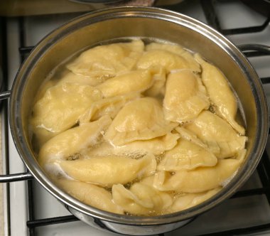 Öğlen üstü, sıcak bir mutfak ortamında, ocağın üstünde, görünen buharlı bir tencerede hamur köftesi kaynıyor.