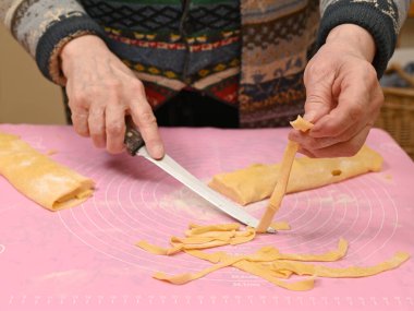 Sıcak bir mutfak ortamında makarnayı ustalıkla şekillendiren ve kesen bir kadın. Tezgah un ve makarna şeritleriyle kaplı. Yemek pişirmeye hazırlanıyorlar.