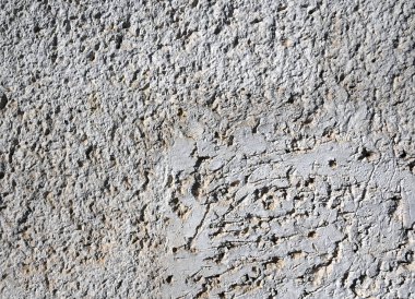 Erozyondan oluşan karmaşık desenleri vurgulayan desenli beton duvarın yakın görüntüsü. Güneş ışığı pürüzlü yüzeyi güçlendirir ve griliğin çeşitli tonlarını ortaya çıkarır.