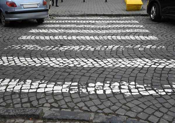 Пешеходный переход с уникальным узорчатым тротуаром и припаркованными автомобилями на булыжной улице в городе