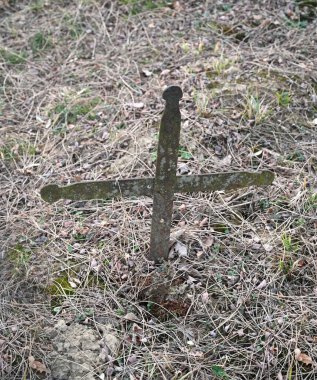 Eski demir haç, terk edilmiş bir mezarlıkta uzun otların ve düşen yaprakların arasına yerleştirilmiştir.