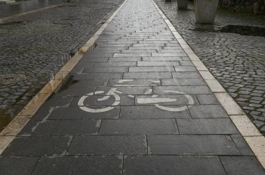 Sakin bir şehirde, ıslak bir kaldırım taşının üzerinde bisiklet yolu işaretli.