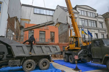 Uzhhorod, Ukrayna - 14 Mart 2025: Otel rekonstrüksiyonu sırasında bir inşaat alanında ağır ekipman taşıyan büyük vinç. İşçiler görev ilerledikçe uzaktan izlerler 