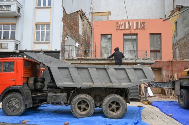 Uzhhorod, Ukrayna - 14 Mart 2025: İnşaat ekibi şehir ortamındaki yıkılmış bir yapının enkazlarını temizliyor. Atık maddelerin taşınması için bölgeye yakın bir yere park edilmiş bir kamyon var.