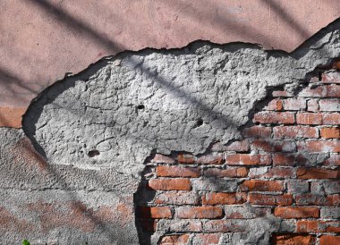 Öğleden sonraları gölgelerle vurgulanan alçı ve tuğlaları soyan eski bir duvar sergisi. Dokular zamanın geçişini gösteriyor. 