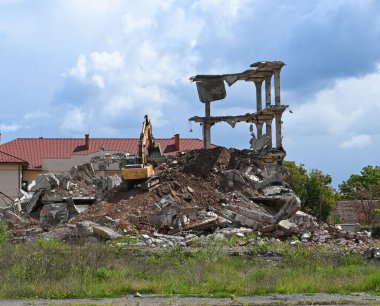 Uzhhorod, Ukrayna - 12 Mayıs 2025: Ağır makineler bir yıkım alanında özenle çalışıyor, bir binanın kalıntılarını yıkıyor. Parçalı bulutlu bir gökyüzünün altında enkazın etrafındaki düzensizlik devam eden inşaat çalışmalarını ortaya çıkarıyor.