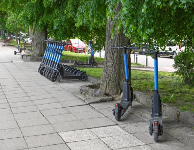Uzhhorod, Ukrayna - 12 Mayıs 2025: Uzhhorod 'da güneşli bir günde ağaçlık kaldırım boyunca düzgün park etmiş elektrikli scooterlar