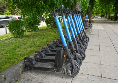 Uzhhorod, Ukrayna - 12 Mayıs 2025: Elektrikli scooterlar Uzhhorod 'da güneşli bir günde yeşil ağaçların altındaki kaldırımda dizildi