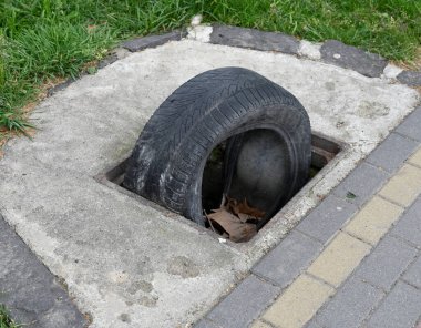 Siyah lastik bir şehir parkındaki beton kanalına kısmen sıkışmış. Bölgeyi çevreleyen çimenler, yakınlarda bulunan yapraklar alışılmadık bir şehir manzarası oluşturuyor.