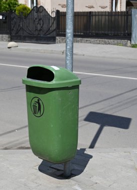 Yeşil çöp kutusu güvenli bir şekilde kaldırım boyunca metal bir direğe monte edilmiştir.