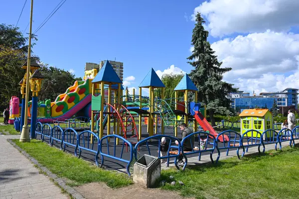 Uzhhorod, Ukrayna - 12 Mayıs 2025: Renkli oyun yapıları çocukları bir şehir parkına çekiyor. Çocuklar slaytları, duvarlara tırmanmayı ve yeşilliklerle çevrili salıncakları keşfederken aileler güneşli havanın tadını çıkarıyor.