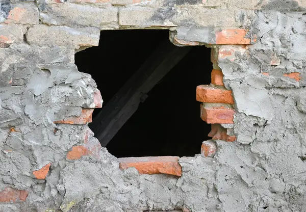 Yıpranmış tuğla duvarda belirgin bir delik, arkasındaki ahşap kirişleri ortaya çıkarıyor. Yapı, doğal ortamdaki kırık tuğlalar ve pürüzlü alçıyla yaş belirtileri gösteriyor.