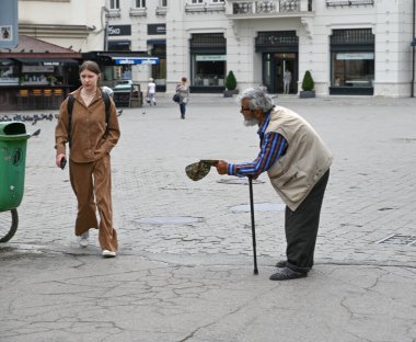 Uzhhorod, Ukrayna - 17 Haziran 2025: Genç bir kadın gün boyunca Uzhhorod 'da bir şehir meydanında yürürken yaşlı bir adam yardım için yalvarıyor
