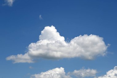 Yumuşak beyaz bulutlar canlı mavi bir gökyüzünde huzur içinde süzülür, sakin bir atmosfer yaratır.