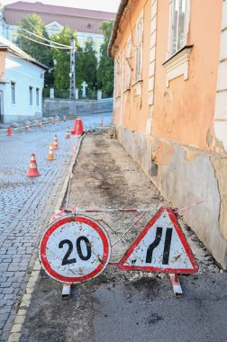 Uyarı levhalarıyla işaretlenmiş dar bir sokakta inşaat faaliyetleri devam ediyor.