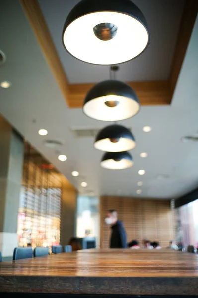 Selective focus on the edge of wooden table in the cafe with blurred modern interior design room and people in background