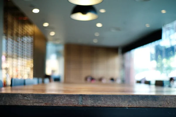 Selective focus on the edge of wooden table in the cafe with blurred modern interior design room and lighting lamps in background