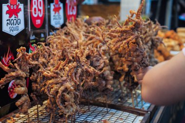 Ahşap çubuklarda kızartılmış kalamar grubu sokak yemeklerinde satıyor. Tayca İngilizce mürekkep balığı anlamına gelir.