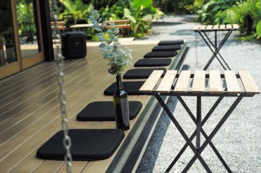 Şarap şişesindeki çiçek buketi ahşap zeminde boş koltuklar ve bahçede bulanık ağaçlarla süslenmiş.