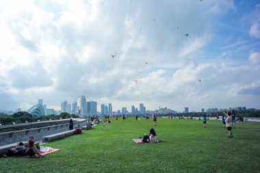 Singapur, Marina yaylım ateşi: 20 Ağustos 2023 - Bir grup insan açık hava parkındaki mavi gökyüzü arka planlı çimenlikte uçurtma oynuyorlar