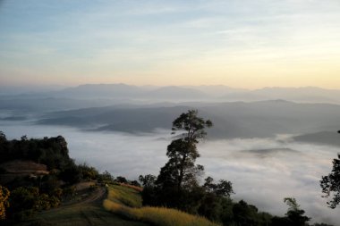 Dağlar arasında kabarık beyaz sis ve arka planda turuncu gün doğumu gökyüzü ile Panorama manzaralı dağ katmanları