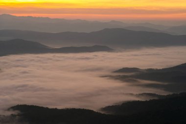 Dağlar arasında kabarık beyaz sis ve arka planda turuncu gün doğumu gökyüzü ile Panorama manzaralı dağ katmanları