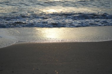 Islak sahildeki güneş ışığının yansıması. Arka planda dalgalar bulanık bir şekilde kıyıya vuruyor.
