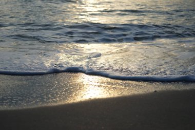 Suyun yüzeyindeki güneş ışığının yansımasıyla kumsalda sörf yapan yakın dalga.