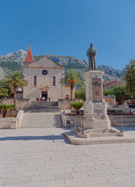 MAKARSKA, CROATIA - 05 Ekim 2019 Andrija Kacic Miosic Anıtı ve ana meydandaki kilise Aziz Mark Kilisesi.