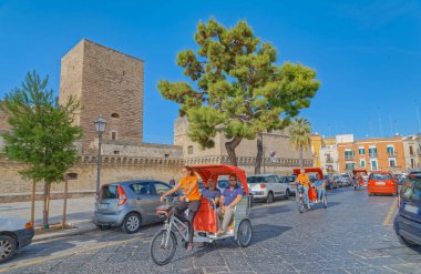 BARI, ITALY - September 26, 2019 Rickshaws passing by the Swabian castle or Castello Svevo, a medieval landmark of Apulia in the city center. clipart