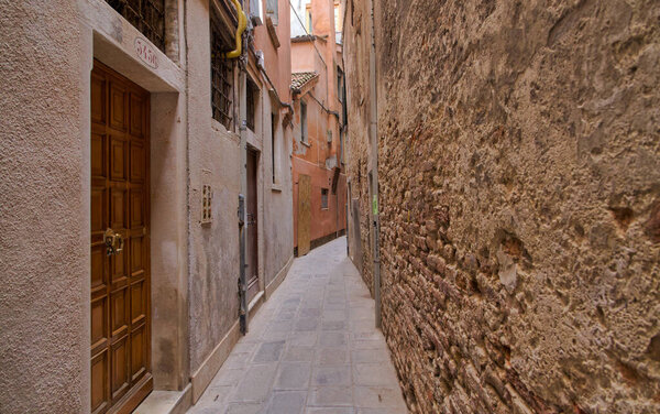 A narrow Venetian alley lined with time-weathered brick walls, exuding the enchanting allure of old-world architecture.