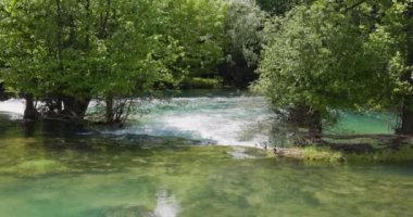 Serene view of the Una River coursing through the bustling city center of Bihac, creating a beautiful juxtaposition of natural beauty and urban life. Slowmotion video.