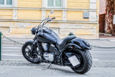 Işıldayan yeni siyah motosiklet yol kenarında güneşli bir kaldırımda duruyor..