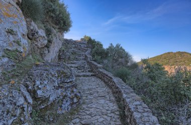 Bir tepenin etrafında kıvrılıp Angelokastros Zirvesi 'ne giden yolu gösteren sarmal adımlar, Angelos Kalesi.