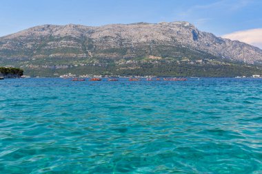 KORCULA, CROATIA - 24 Haziran 2019: Turistli bir grup kano Peljesac yarımadası ve St. Ilija Dağı ile birlikte arka planda süzülüyor.