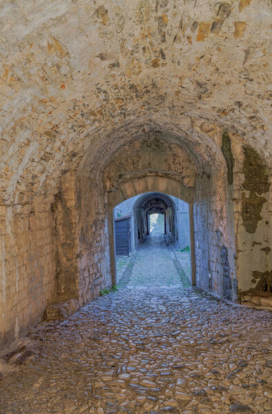 A picturesque interplay of light and shadows at the stone arched entrance of the Rozafa fortress, complemented by a cobblestone pathway.