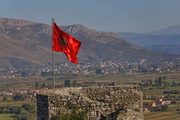 A vibrant Albanian flag waving against the historical backdrop of the Rozafa fortress in Shkoder, capturing a moment of national pride and heritage.